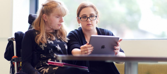 Photo of a woman in a wheelchair examining an iPad with another woman