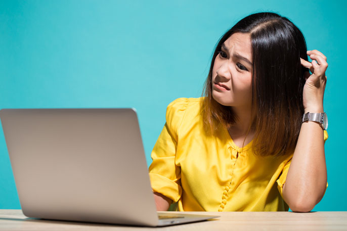 A woman looking at a laptop, scratching her head in confusion.