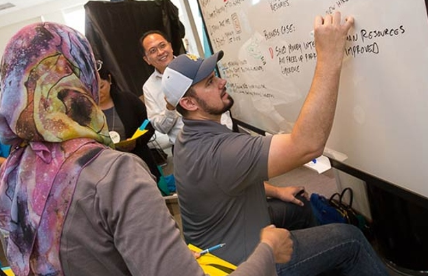 Process Palooza, a participant writes on the whiteboard as others look on.