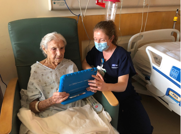 A nurse helps an elderly patient read a tablet in the hospital