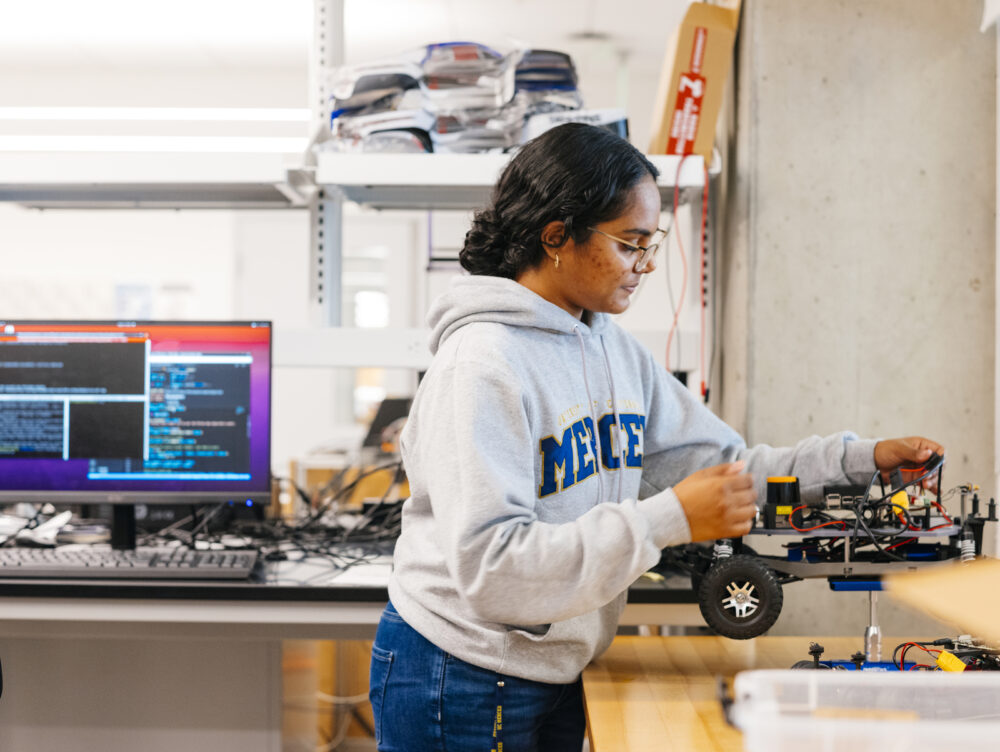 Amrita Mohandas, a 2023 CITRIS Workforce Innovation intern, adjusts a four-wheeled robot used for forestry research in UC Merced professor Ricardo de Castro's laboratory."